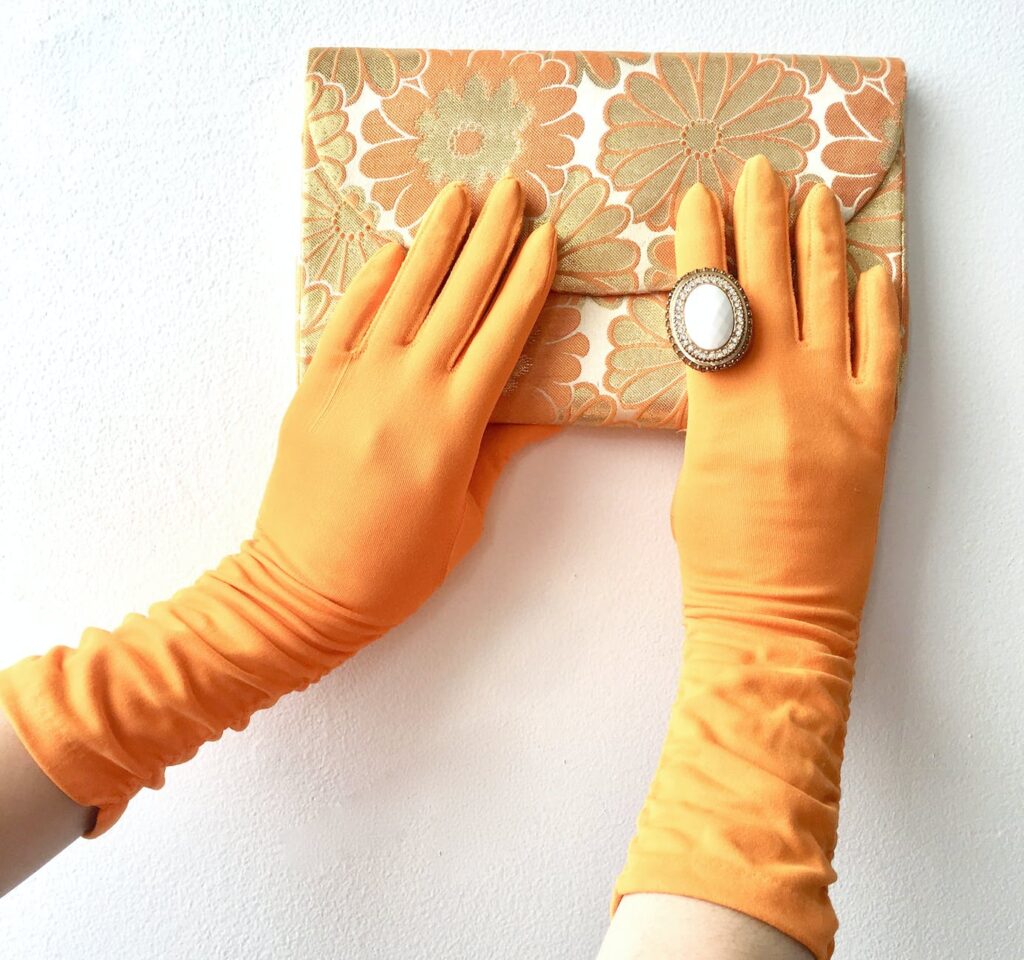 person in yellow gloves holding a floral clutch bag