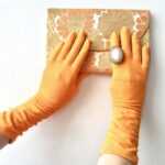 person in yellow gloves holding a floral clutch bag